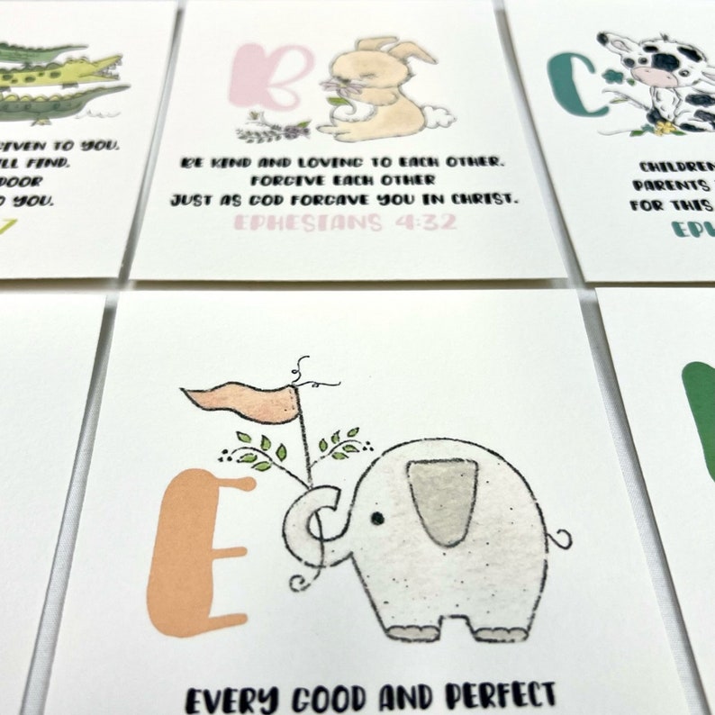 Op de afbeelding: Een set alfabetkaarten met illustraties van dieren en inspirerende citaten. De letter E heeft een perzikkleurige letter met een kleine olifant die een vlag vasthoudt.