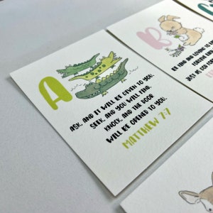 Op de afbeelding: Een groene en gele letter A met een stapel van drie groene alligators. De tekst "ASK. AND IT WILL BE GIVEN TO YOU. SEEK, AND YOU WILL FIND. KNOCK, AND THE DOOR WILL BE OPENED TO YOU. MATTHEW 7:7" staat onder de alligators.