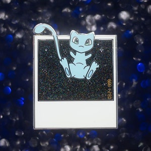 May include: A light blue enamel pin featuring a cartoon character, set against a starry background within a white frame. The pin has a silver border and the character is in a sitting pose. The text "03.24.699" is visible.