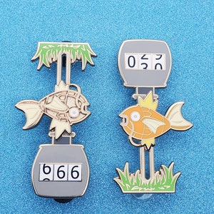 May include: Two metal pins with fish designs. One pin shows a fish with the number "666" on a counter, and the other shows a fish with the number "052" on a counter. Both pins have green and gold accents.