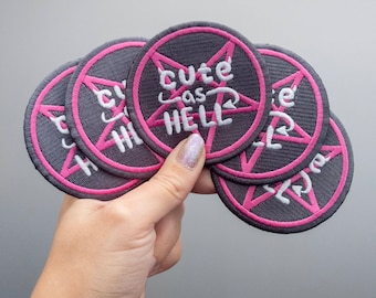 Może przedstawiać: Kolekcja ciemnoszarych, okrągłych naszywek z różowym pentagramem i białym napisem "cute as HELL". Naszywki są trzymane w dłoni na jasnoszarym tle.