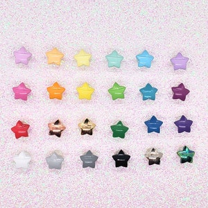 May include: A collection of star-shaped beads in various colors, including pink, orange, yellow, green, blue, and purple. Some beads have a metallic finish in gold, silver, and copper. The beads are arranged on a glittery pink surface.