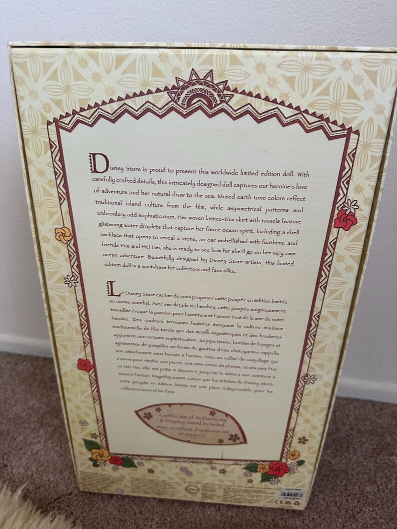 May include: A limited edition Moana doll from Disney Store. The doll is wearing a brown and white woven skirt with tassels, a shell necklace, and a red flower in her hair. The box features a brown and white background with text in English and French.