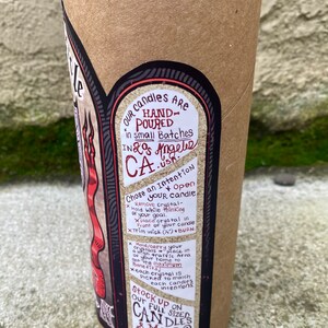 Pode incluir: Um tubo de cart&atilde;o castanho com um r&oacute;tulo preto que apresenta uma ilustra&ccedil;&atilde;o vermelha e preta de uma vela. O r&oacute;tulo inclui o texto "Nossas velas s&atilde;o feitas &agrave; m&atilde;o em pequenos lotes em Los Angeles, Calif&oacute;rnia." e instru&ccedil;&otilde;es para usar a vela com cristais. O r&oacute;tulo tamb&eacute;m inclui o texto "Abaste&ccedil;a-se de nossas velas de tamanho completo e mais @ www.psychiccirclecandles.com".
