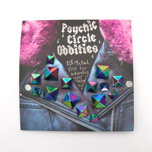 May include: A card with the text "Psychic Circle Oddities" and "15 Metal Pins for Adorning Your Things" with a black leather jacket with rainbow iridescent pyramid-shaped studs.