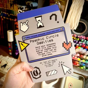 May include: A gray and blue computer-themed notepad with the text "Psychic Circle Oddities." The notepad features pixelated icons and the text "New unread message received.exe." Includes 48 tear-off sheets and a sticker page with 18 stickers.