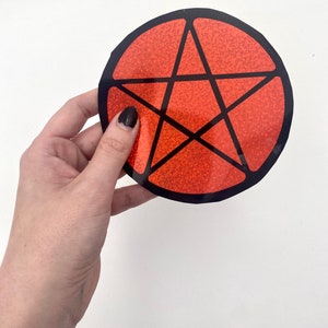 May include: A red pentagram sticker with a black outline. The sticker is made of glitter and has a shiny finish.