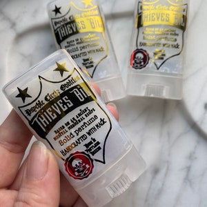 Può includere: Due tubi di plastica trasparente con lettere dorate che recitano "Psychic Circle Oddities Thieves Oil" e "Basato su un'antica ricetta medicinale medievale. Profumo solido. Realizzato a mano con la magia." I tubi hanno un adesivo rosso con teschio e ossa incrociate sul fondo.
