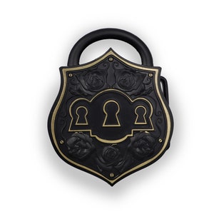 May include: Black decorative padlock with a shield-shaped design. The padlock features a black finish with gold accents, including keyholes and rose motifs. The handle is black and arched.