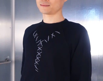 以下が含まれることがあります： 前面に白いステッチのデザインが施された黒い長袖シャツ。シャツはクルーネックで、柔らかく快適な生地で作られています。