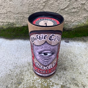 Pode incluir: Um tubo de cart&atilde;o castanho com uma tampa preta. O tubo tem um r&oacute;tulo com uma ilustra&ccedil;&atilde;o em preto e branco de um olho dentro de um escudo. O r&oacute;tulo tamb&eacute;m diz "Psychic Circle Oddities Candle Set" e "4 - 4 oz Soy Candles".