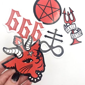 May include: Five red and black stickers with a satanic theme. The stickers include a pentagram, a goat head, a trident, the number 666, and a symbol with a cross and an infinity sign. The trident sticker has the words "Hail Satan" on a banner.