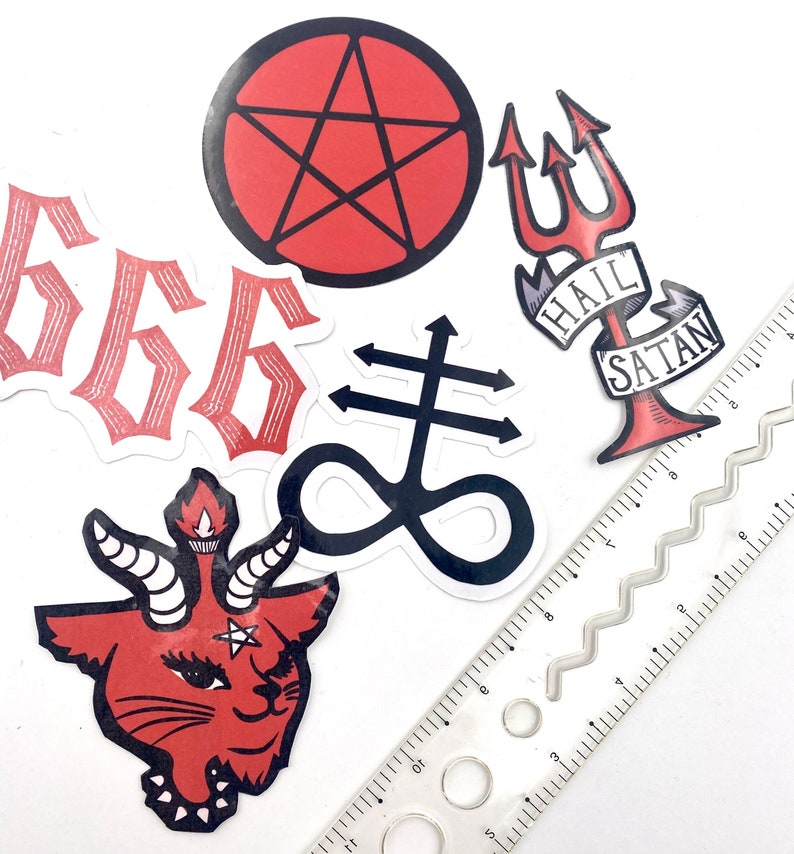 May include: A set of six red and black stickers with various satanic symbols, including a pentagram, an upside-down cross, a trident, and the number 666. The stickers are arranged on a white surface with a ruler.