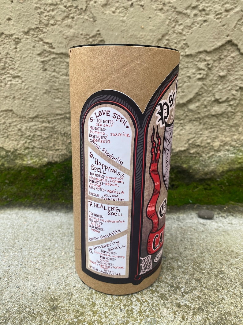 Pu&ograve; includere: Un tubo di cartone marrone con un'etichetta nera e rossa. L'etichetta presenta un'illustrazione in bianco e nero di una ragnatela e un nastro rosso con il testo "Candle Spell". L'etichetta include anche un elenco di diversi incantesimi con le loro note di cristallo e profumo corrispondenti. Gli incantesimi includono Love Spell, Happiness Spell, Healing Spell e Prosperity Spell.