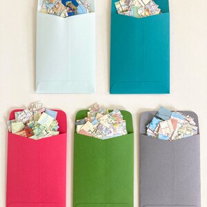 May include: Five envelopes, each filled with colorful confetti made from maps. The envelopes are light blue, teal, red, green, and gray.