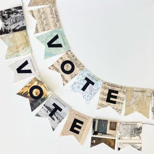 May include: A decorative bunting banner featuring swallowtail flags crafted from vintage paper, including maps and sheet music. The flags are strung together with black and white twine, spelling out the word VOTE in bold, black, capital letters.