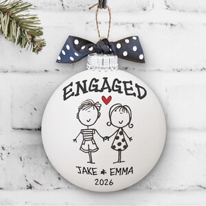 Whimsical engaged couple artwork with "Engaged" written above couple and first names and 2026 below.