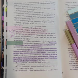 May include: Open book with text, highlighted passages, and colorful sticky notes. A pink and gold pen rests on the page. The book is open to page 210, with the title "FOURTH WING" at the top.