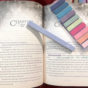 May include: Open book with Chapter 37 visible, highlighted text, and colorful sticky notes. A light purple highlighter and a pack of rectangular sticky notes in various colors are on the pages. The book is open on a dark surface.