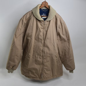 May include: A tan quilted jacket with a zipper closure and a cream colored knit collar. The jacket has a blue lining and ribbed cuffs.