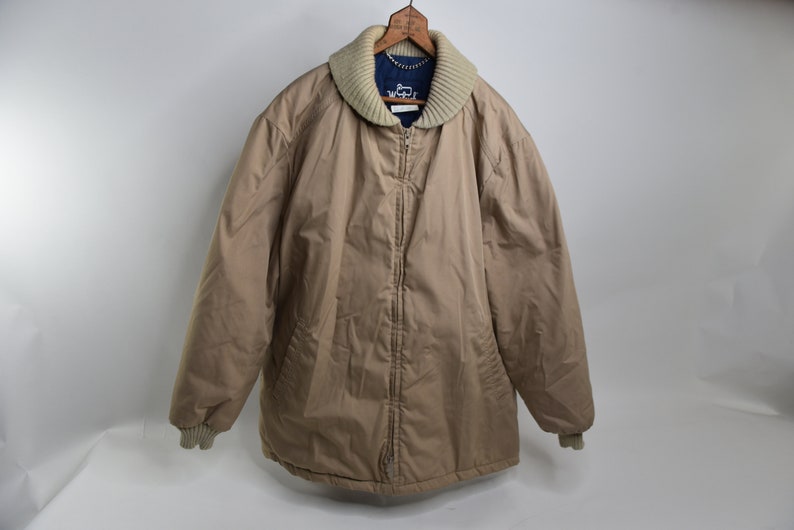 May include: A tan quilted jacket with a zipper closure and a cream colored knit collar. The jacket has a blue lining and ribbed cuffs.