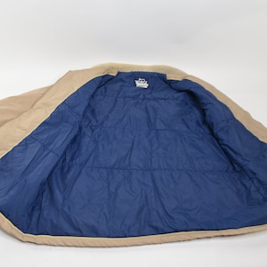 May include: A tan puffer jacket with a blue quilted lining. The jacket is unzipped and laid flat.