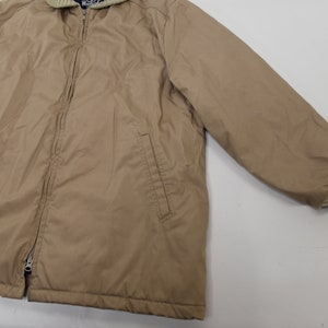May include: A tan zip-up jacket with a ribbed knit collar and cuffs. The jacket has two pockets on the front and a zipper closure.