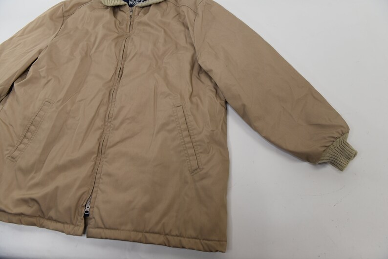 May include: A tan zip-up jacket with a ribbed knit collar and cuffs. The jacket has two pockets on the front and a zipper closure.