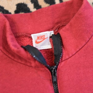May include: A red Nike sweatshirt with a black zipper and a white Nike logo tag that says "Nike" and "Made in USA".