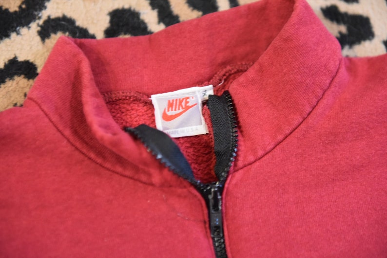 May include: A red Nike sweatshirt with a black zipper and a white Nike logo tag that says "Nike" and "Made in USA".