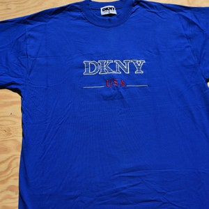 May include: A royal blue t-shirt with a white embroidered DKNY logo and the words "USA" in red.