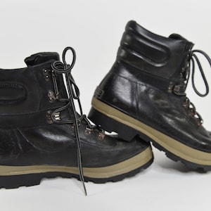 May include: A pair of black leather hiking boots with a brown rubber sole. The boots have a lace-up closure and a padded collar.