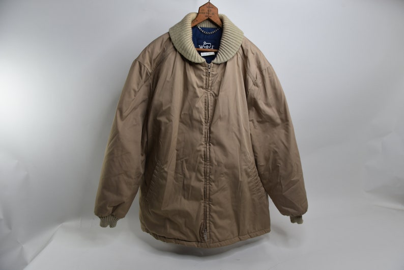 May include: A tan quilted jacket with a zipper closure and a ribbed knit collar. The jacket has a blue label with the text "Weatherproof" on the front.