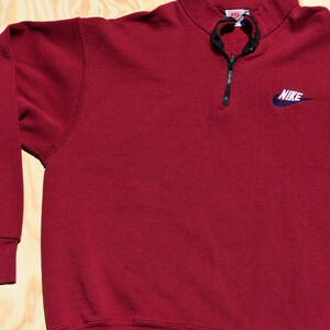 May include: A maroon 1/4 zip sweatshirt with a navy blue Nike logo on the left chest.