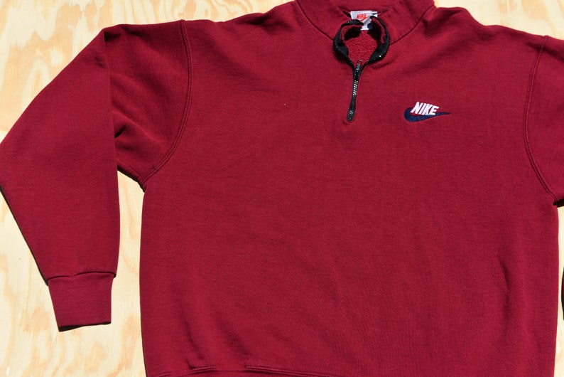 May include: A maroon 1/4 zip sweatshirt with a navy blue Nike logo on the left chest.