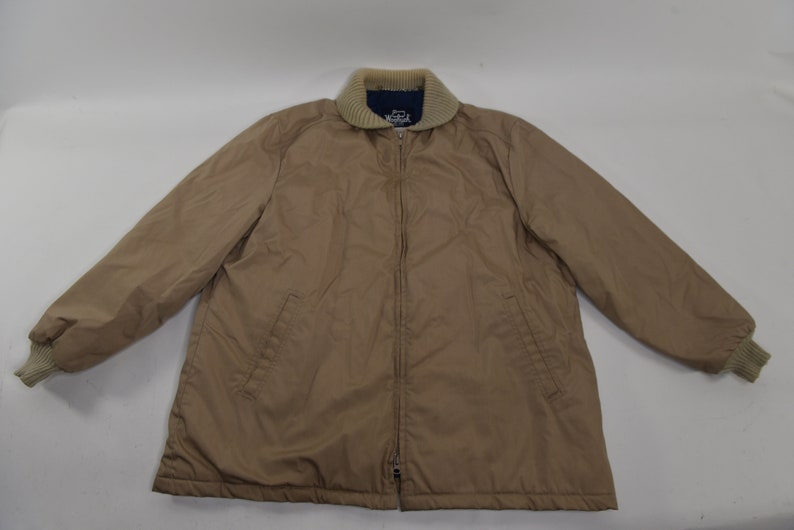 May include: A tan zip-up jacket with a brown knit collar and cuffs. The jacket has two pockets on the front and a zipper closure.