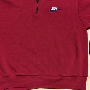 May include: A maroon 1/4 zip sweatshirt with a small embroidered Nike logo on the left chest.