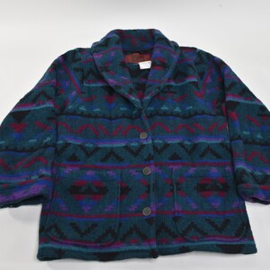 Puede incluir: Una chaqueta de forro polar con estampado de color verde azulado, morado y rojo con cuello chal y cierre de botones. La chaqueta tiene dos bolsillos en la parte delantera.