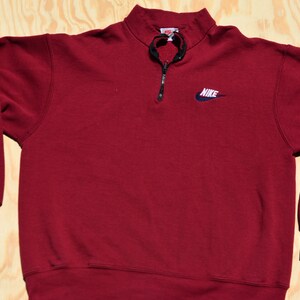 May include: A maroon 1/4 zip sweatshirt with a navy blue Nike logo on the front.