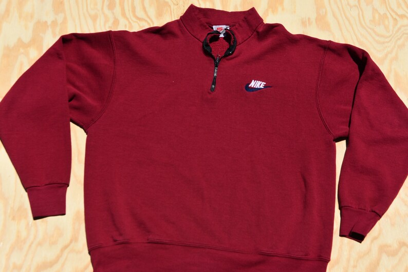 May include: A maroon 1/4 zip sweatshirt with a navy blue Nike logo on the front.