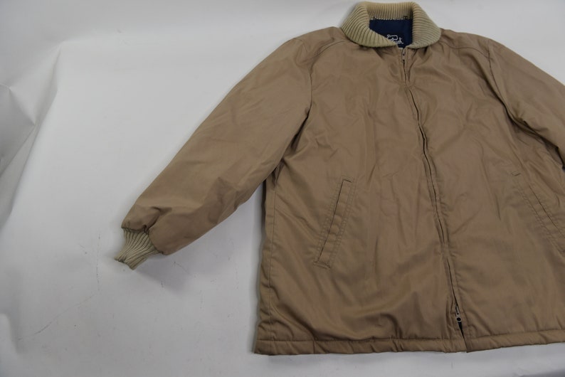 May include: A tan zip-up jacket with a ribbed collar and cuffs. The jacket has a zipper closure and two pockets on the front.