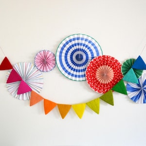 May include: A colorful paper fan garland with red, blue, green, and white paper fans. The garland is decorated with a rainbow felt banner.