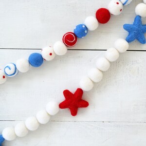 May include: A red, white, and blue felt garland with stars and polka dots. The garland is made of felt balls and is perfect for decorating for a patriotic holiday.