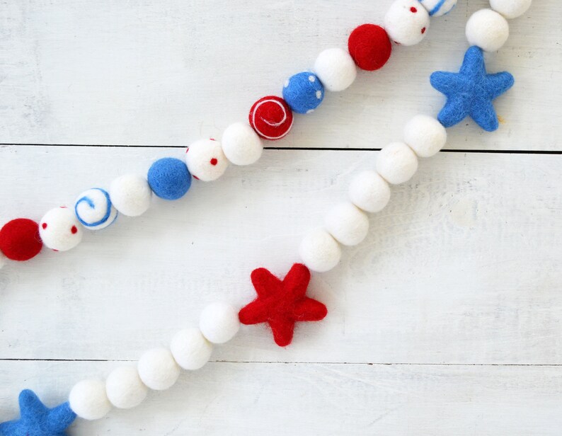 May include: A red, white, and blue felt garland with stars and polka dots. The garland is made of felt balls and is perfect for decorating for a patriotic holiday.