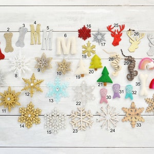 May include: A collection of 38 felt and glitter ornaments in various shapes, including snowflakes, reindeer, trees, bones, seahorses, and rainbows. The ornaments are numbered 1 through 38.