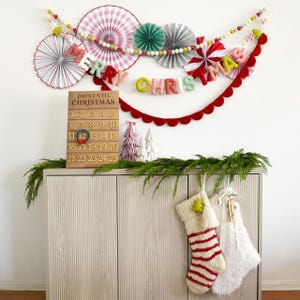 May include: A Christmas display with a garland spelling "MERRY CHRISTMAS", paper fans, and a red scalloped border. A wooden advent calendar and decorative stockings are also visible, creating a festive atmosphere.