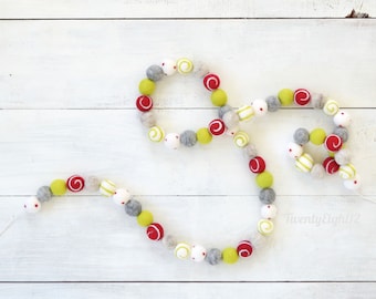 May include: A festive garland made of felt balls in red, white, green, and yellow. The balls have a variety of patterns, including stripes and polka dots. The garland is strung together with a white thread.