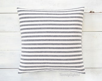 May include: A gray and white striped pillow with a white background and gray stripes. The pillow is on a white wooden surface.
