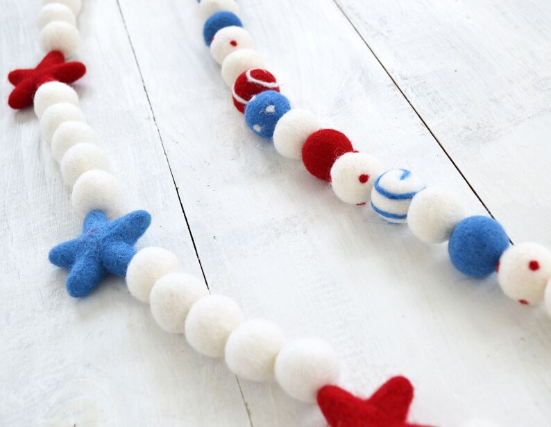 May include: A white, blue, and red felt ball garland with stars and polka dots. The garland is strung on a white background.