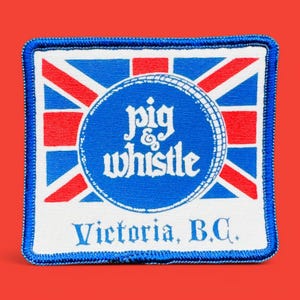 Könnte beinhalten: Ein blauer und weißer gestickter Aufnäher mit einem Union-Jack-Design. Der Aufnäher zeigt einen Kreis mit dem Text "pig & whistle" und den Worten "Victoria, B.C."